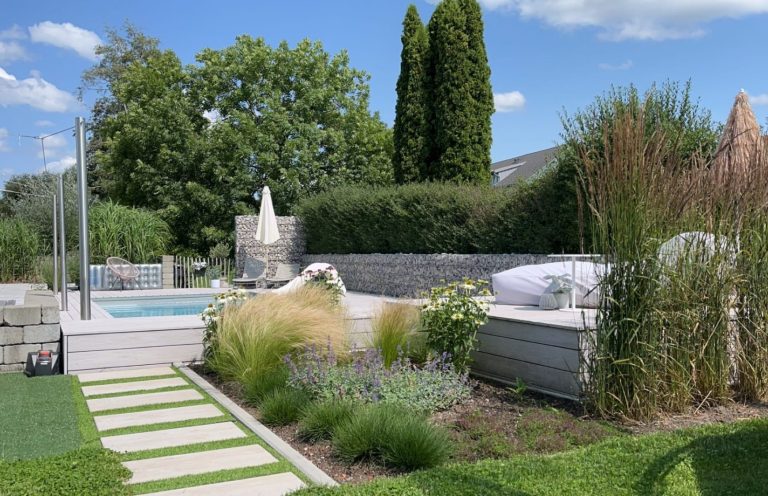 Staudenbeet und Trittplattenweg mit Holzpodest und Pool im Hintergrund